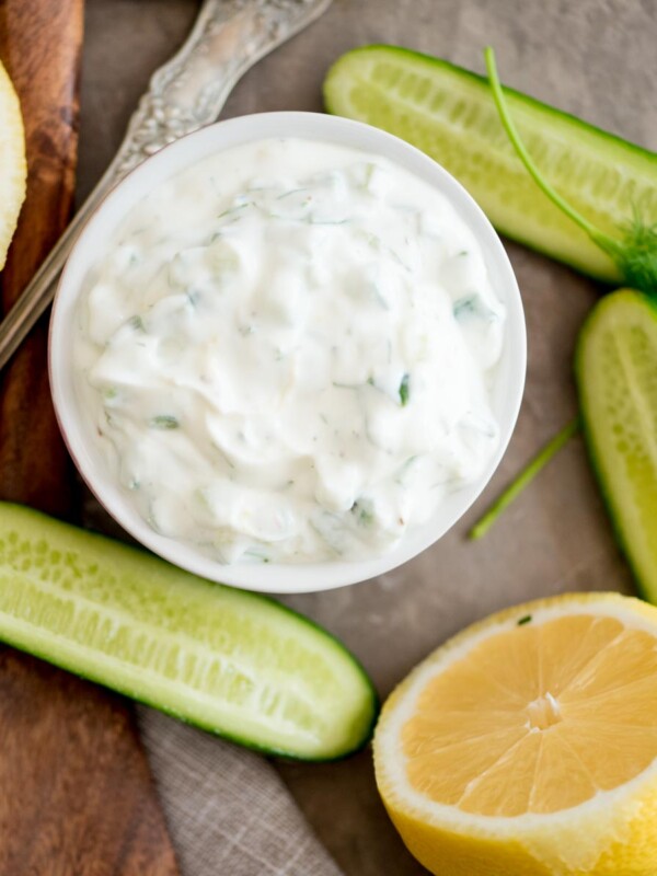 tzatziki sauce in a bowl surrounded by cucumbers and lemon