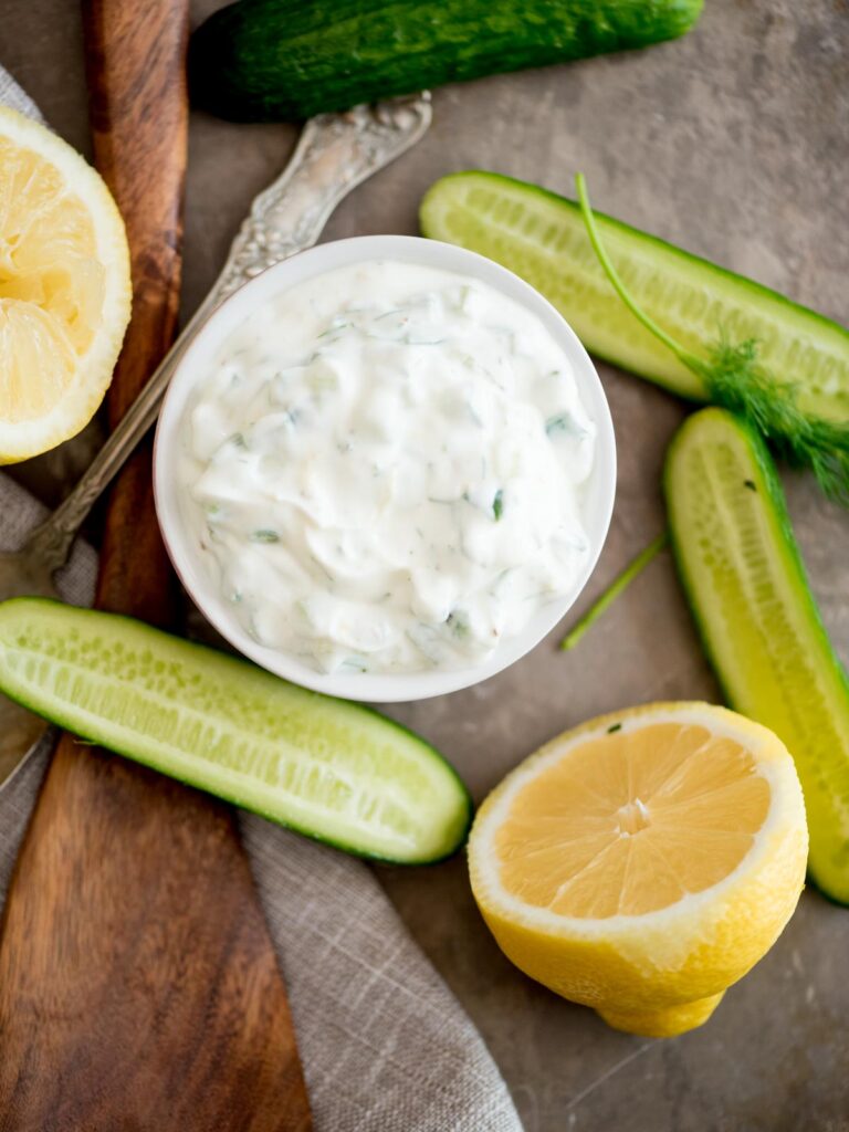 tzatziki sauce in a bowl surrounded by cucumbers and lemons