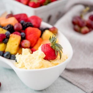 strawberry dipped in yogurt fruit dip with a bowl of fruit