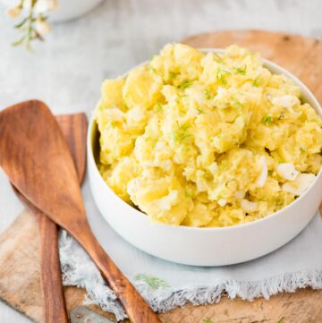 old fashioned potato salad in a white bowl topped with fresh dill