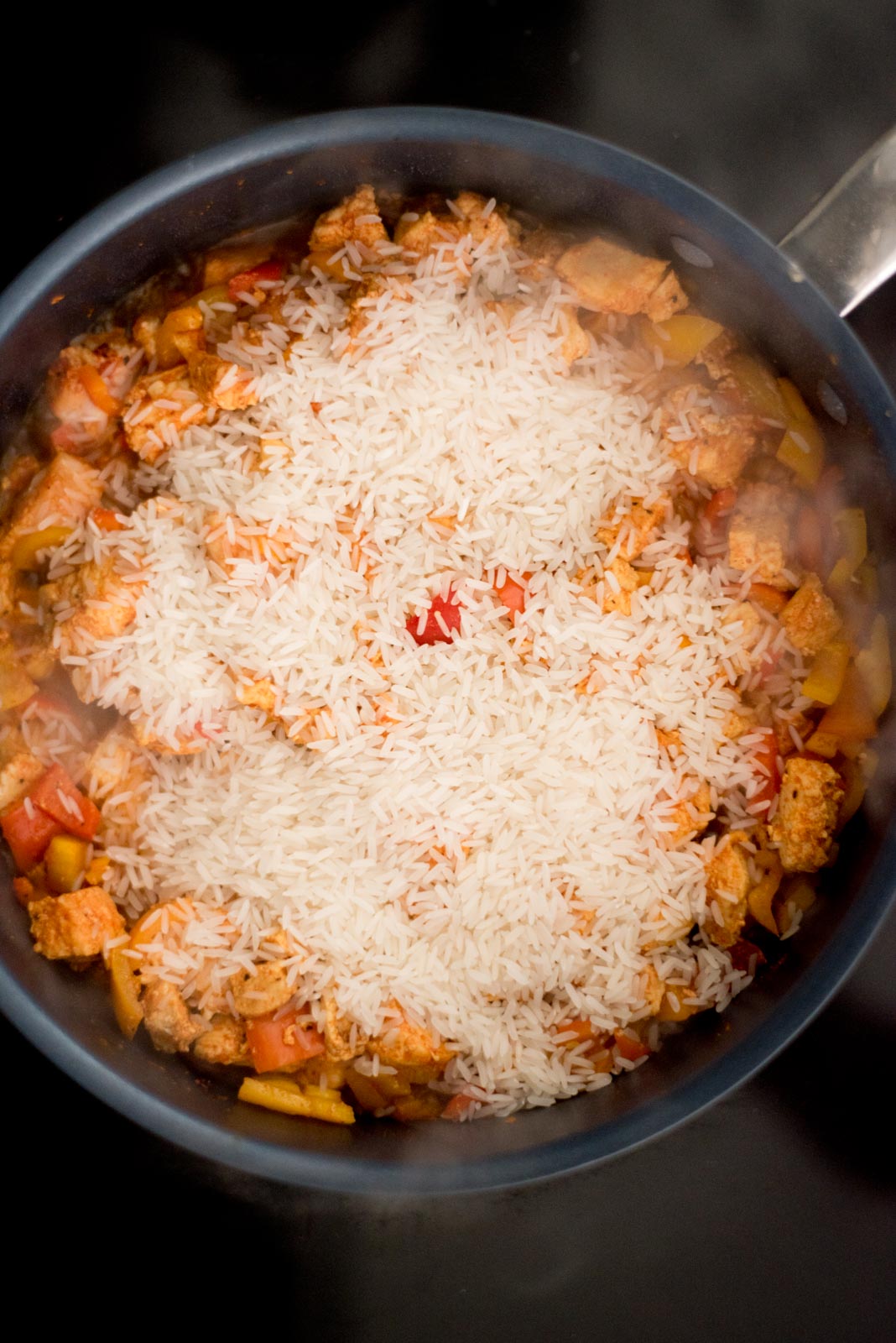 rice added to the skillet on the stove with the cooked chicken and bell peppers