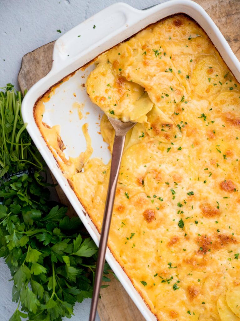 Cheesy au grain potatoes in a baking dish with a serving spoon resting in it. 