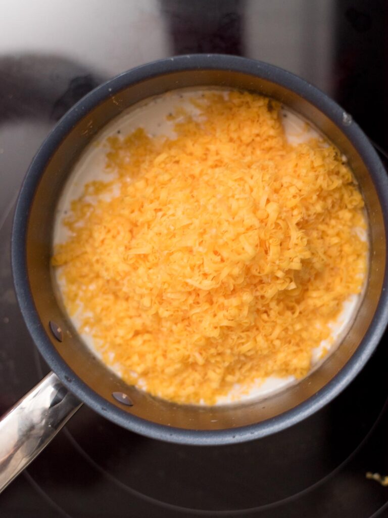 Hand shredded cheese added to a saucepan.