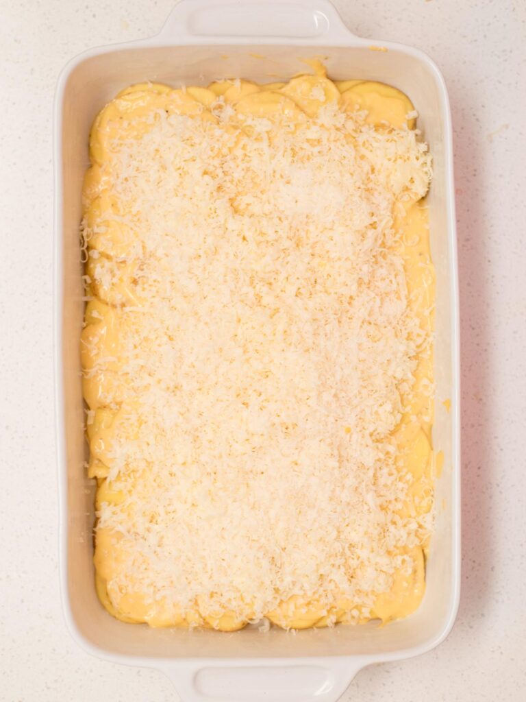Potatoes layered in a casserole dish and topped with grated cheese.