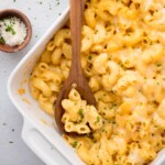 Scoop of mac and cheese taken out of a baking dish with a wooden spoon resting in it.