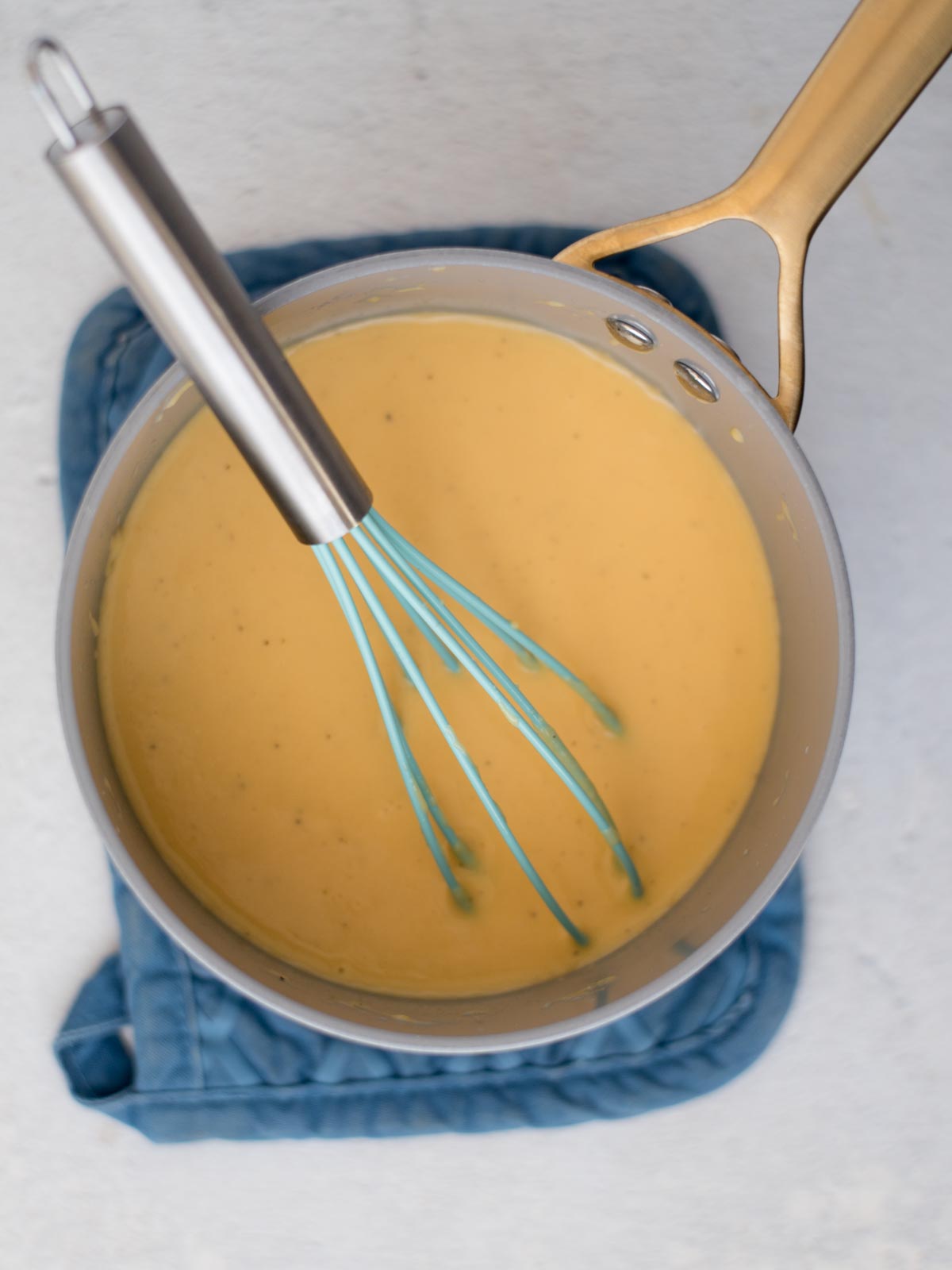 Whisk resting in a saucepan of cheese sauce.