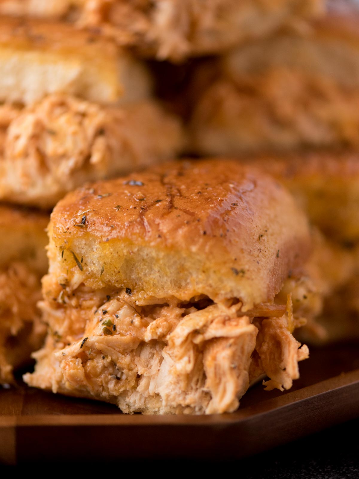 A single buffalo chicken slider with seasoned chicken spilling out sitting on a platter of sliders.