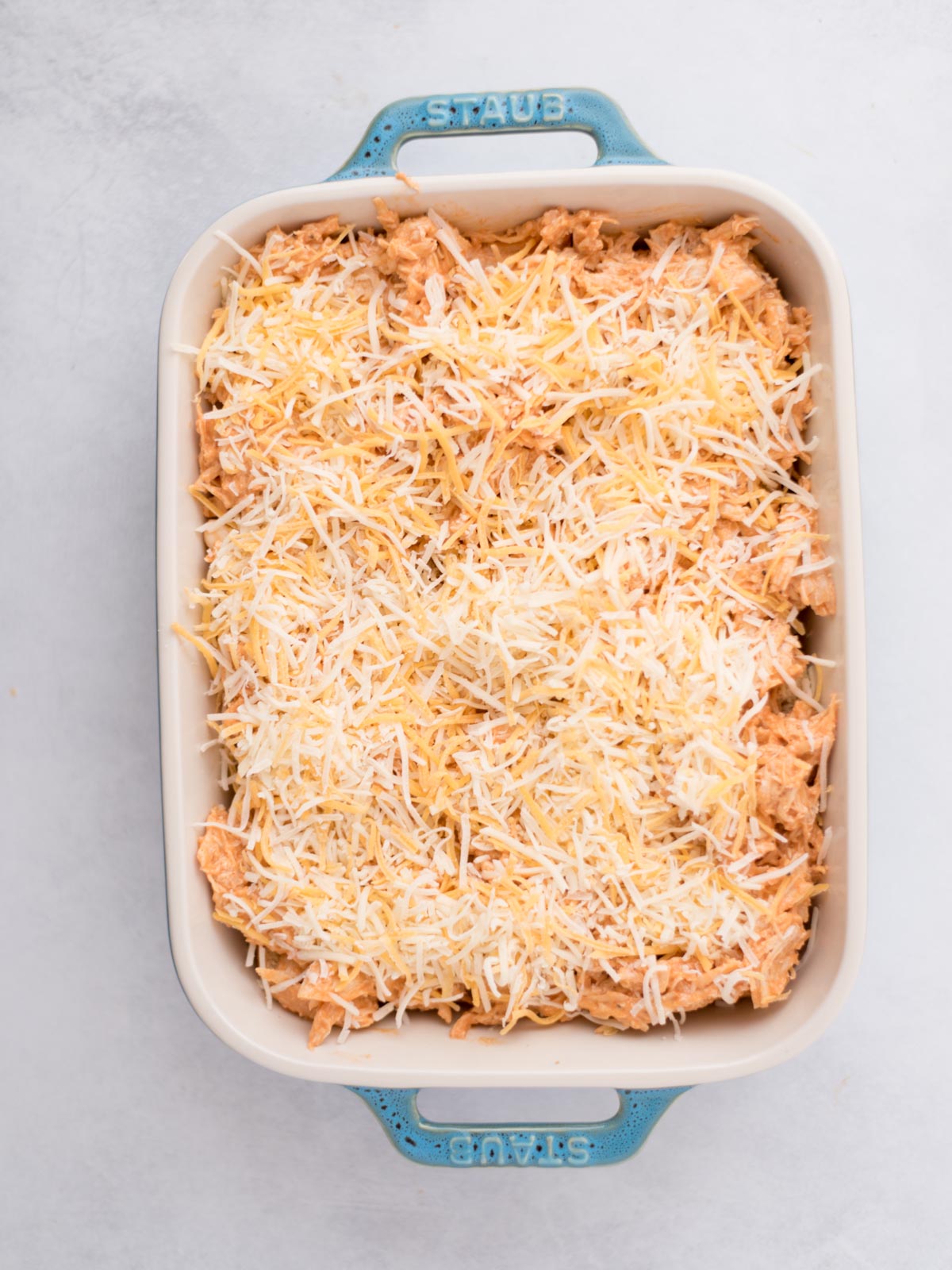 Shredded cheese topping the buffalo chicken sliders in a baking dish.