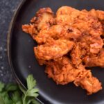 boneless buffalo wings on a black plate with a parsley garnish