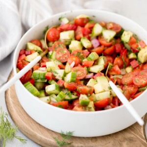 Bowl of cucumber tomato salad with salad tongs ready to use resting in it.