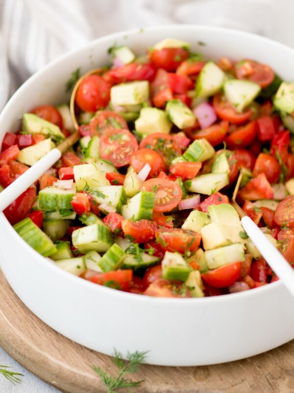 Bowl of cucumber tomato salad with salad tongs ready to use resting in it.