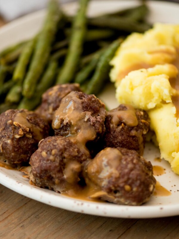 french onion meatballs topped with gravy served on a plate with mashed potatoes and roasted green beans