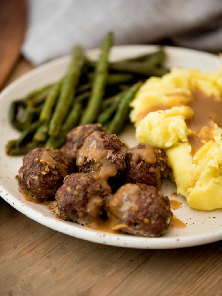 french onion meatballs with gravy served on a plate with mashed potatoes and roasted green beans