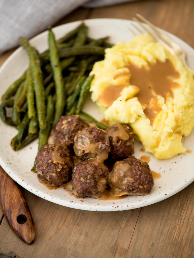 french onion meatballs served on a plate with mashed potatoes, gravy, and roasted green beans
