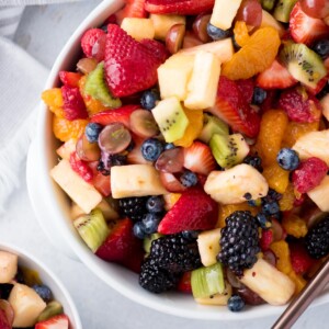 fruit salad with dressing in a while bowl with a serving spoon and a kitchen linen