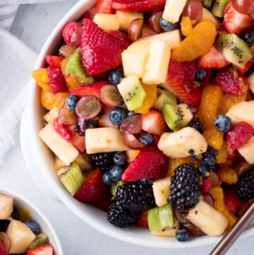fruit salad with dressing in a while bowl with a serving spoon and a kitchen linen