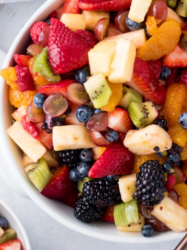 fruit salad with dressing in a while bowl with a serving spoon and a kitchen linen