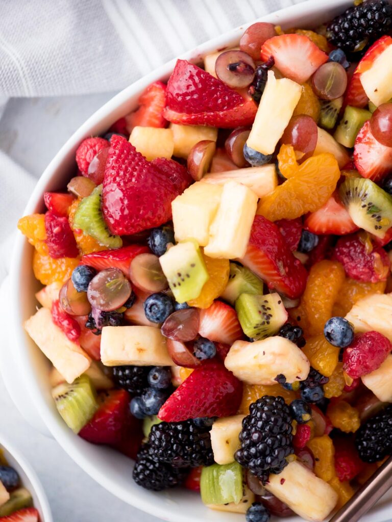 fruit salad in a white bowl with a serving utensil