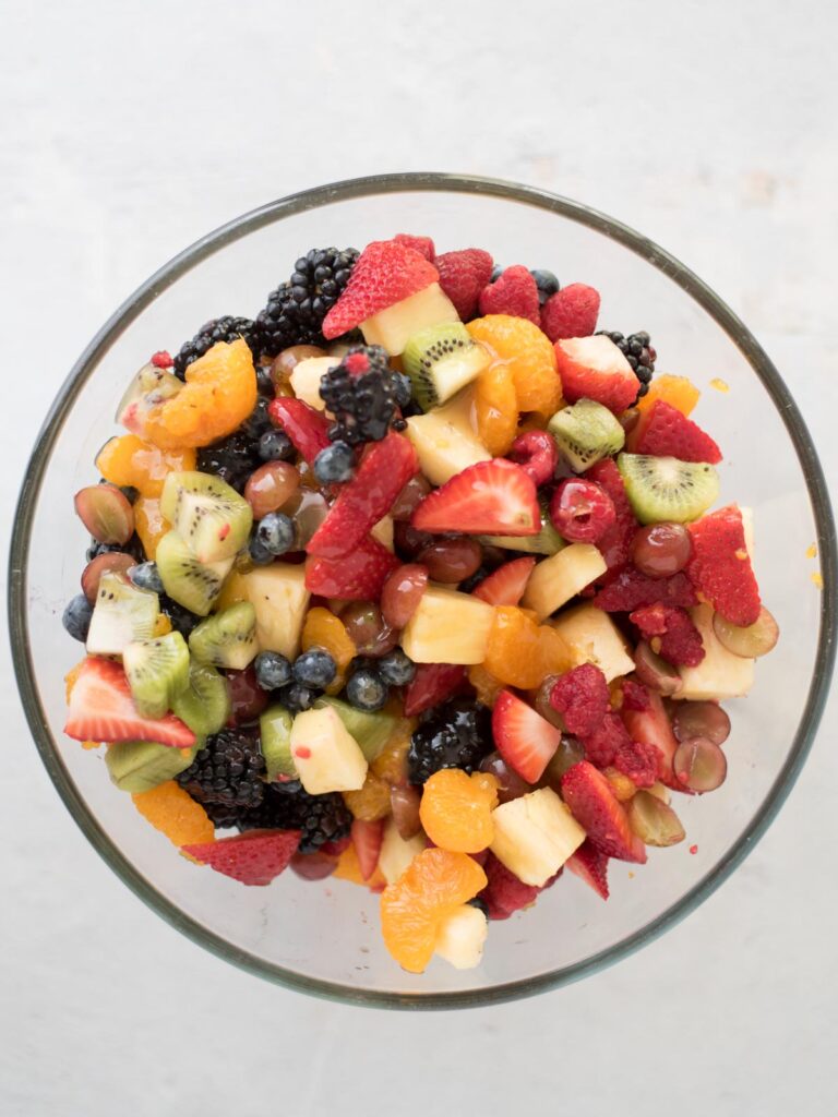 dressing poured on top of mixed fruit in a large mixing bowl