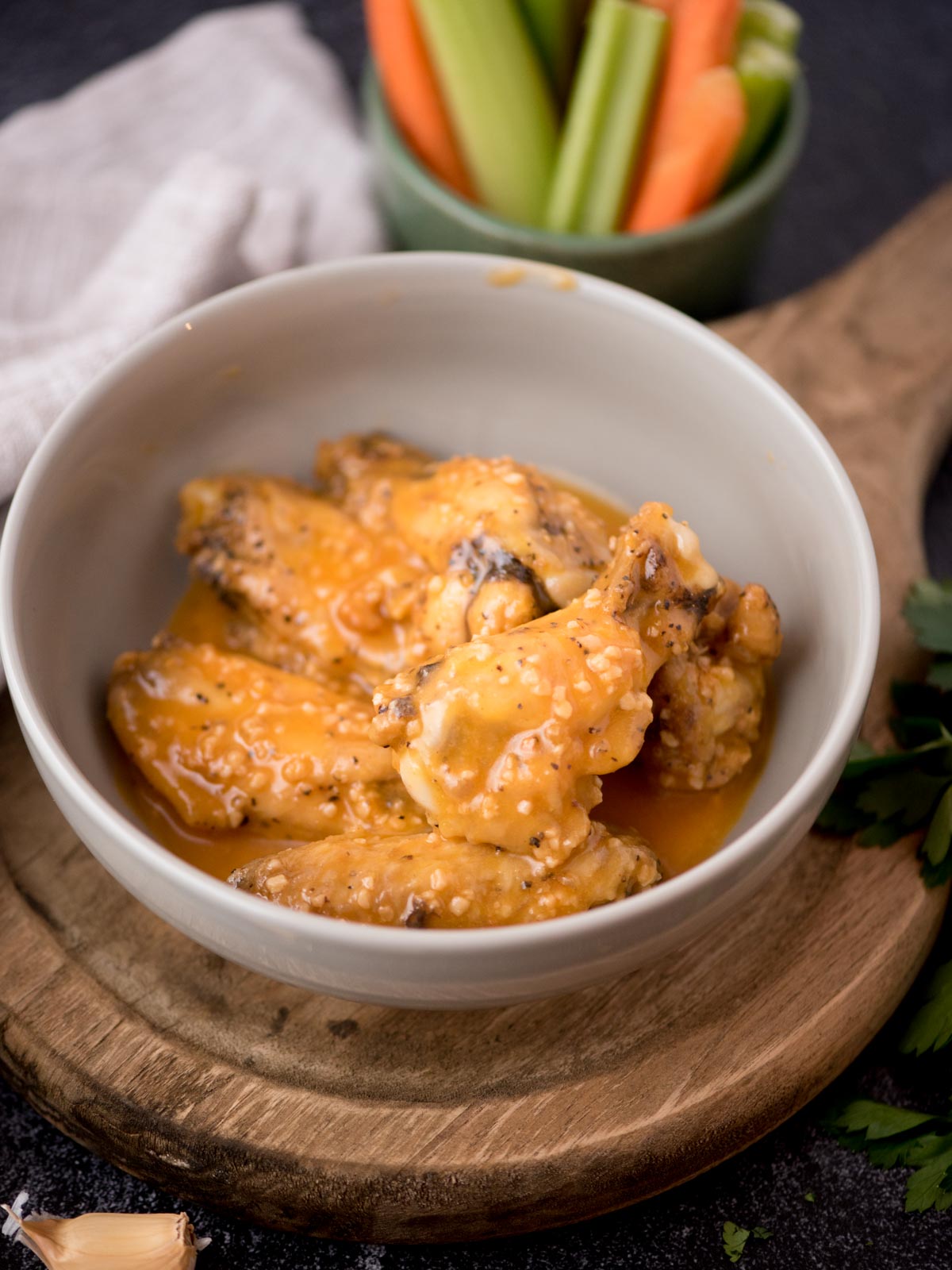 garlic butter chicken wings in a bowl covered in sauce with a small bowl of carrots and celery nearby