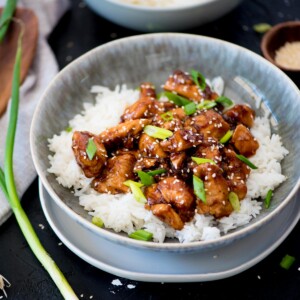 General Tso chicken and rice in a bowl garnished with sliced green onions.