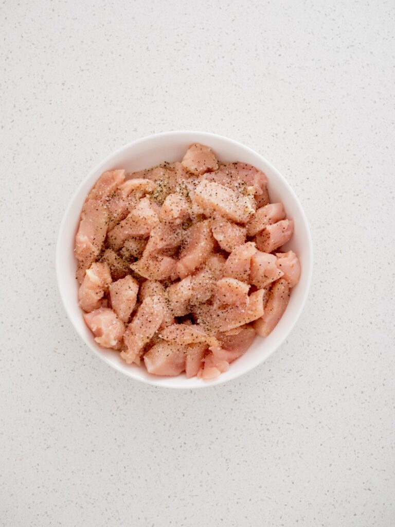 Seasoning sprinkled over raw chicken chunks in a bowl.