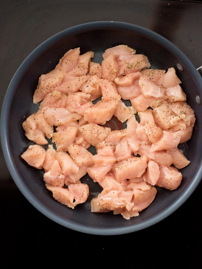 Raw chicken cut into chunks and added to a frying pan.