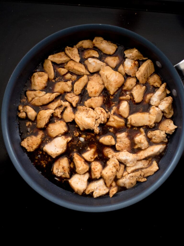 Chicken breast chunks added to a frying pan over General Tso sauce.