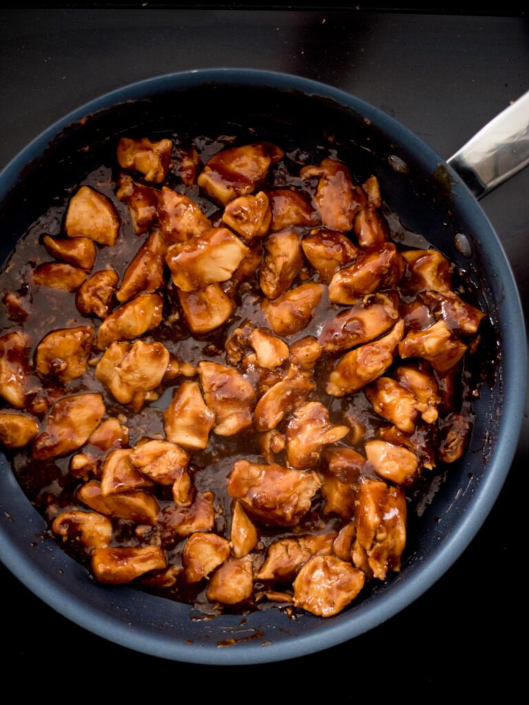 A frying pan with chicken chunks in a General Tso sauce.