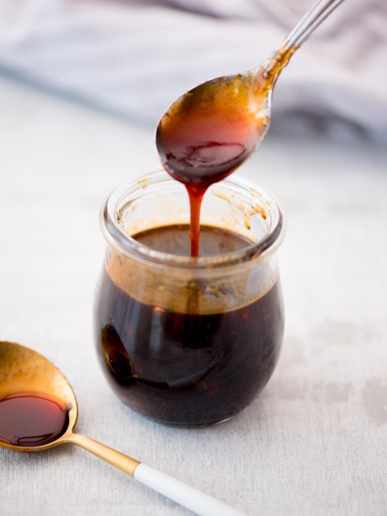Spoon drizzling honey sriracha sauce into a small glass jar.