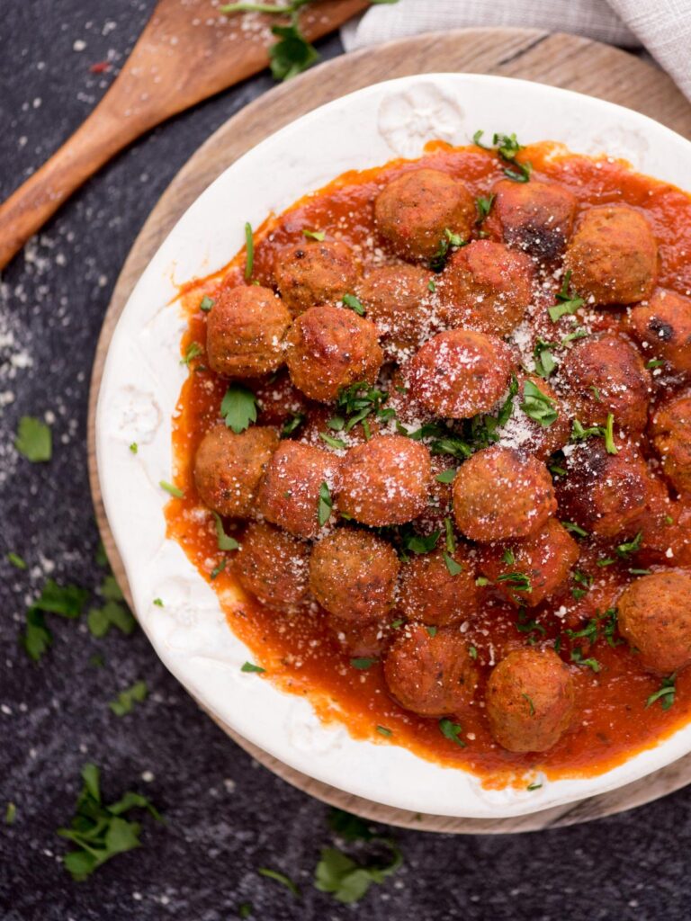 Top view of a bowl of meatballs and tomato sauce with a wooden spoon laying next to it.