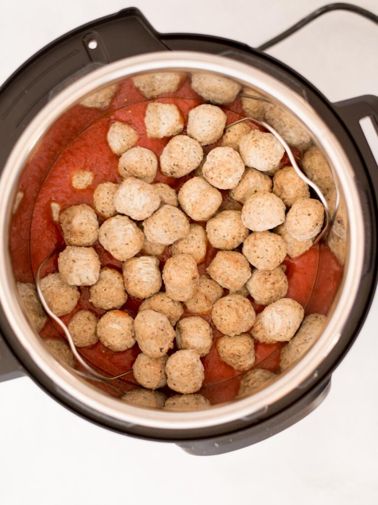 Frozen meatballs over tomato sauce in an instant pot ready to cook.