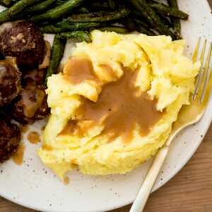 brown gravy on top of mashed potatoes on a plate served with meatballs and green beans