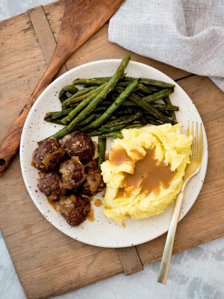 Top view of mashed potatoes and gravy, green beans and french onion meatballs.