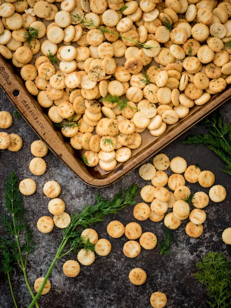 Baking sheet covered in seasoned oyster crackers with sprigs of fresh dill.