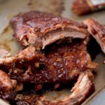 Close up of ribs on a baking sheet with sauce coating them and a few pieces of lean meat pulled away.
