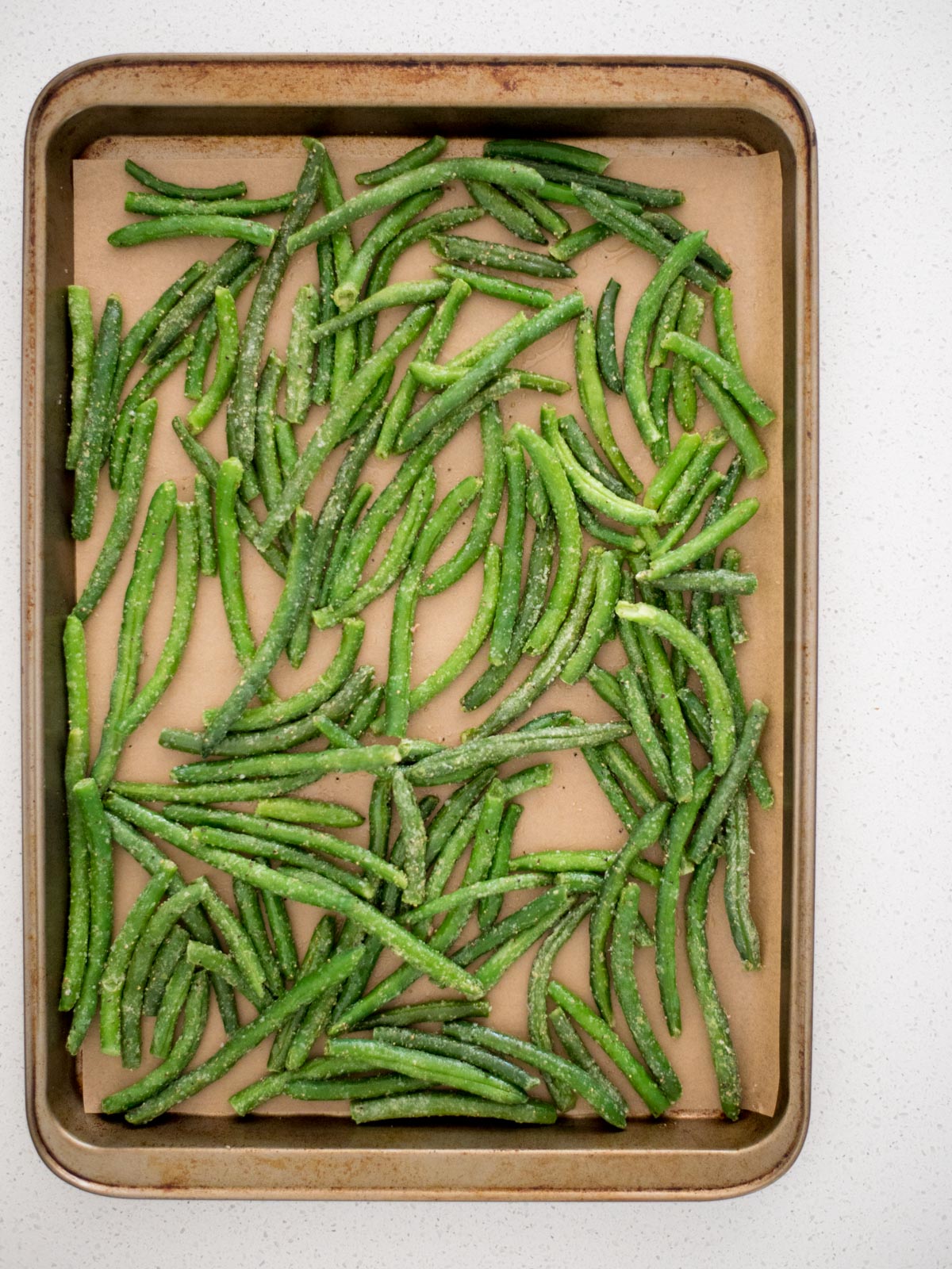 frozen green beans laying on parchment paper on a baking sheet.