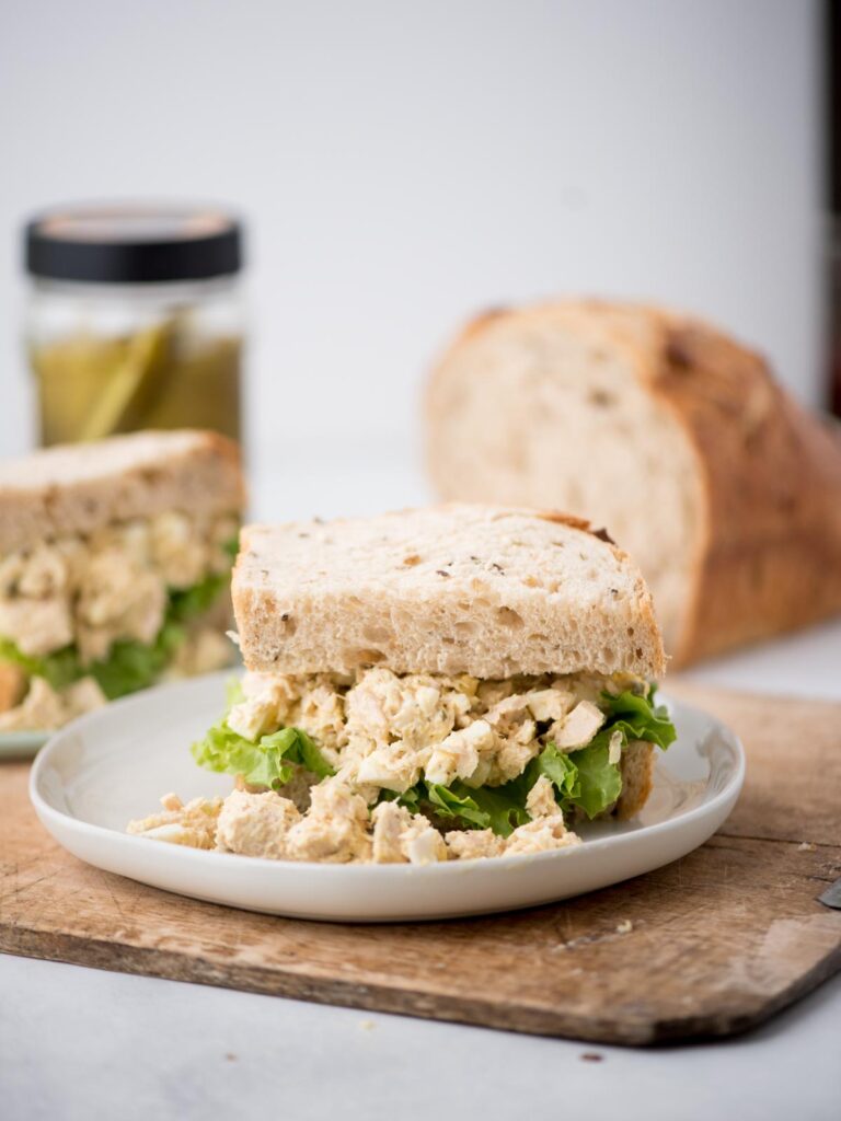 Half a loaf of bread behind a tuna salad sandwich served on a plate.