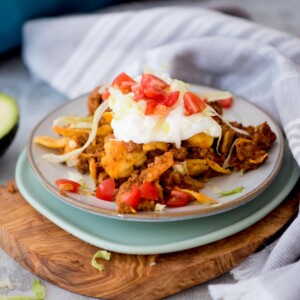 A small plate with a serving of walking taco casserole on it and garnished with sour cream and diced tomatoes.