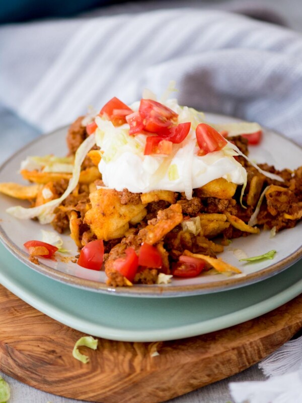 A small plate with a serving of walking taco casserole on it and garnished with sour cream and diced tomatoes.