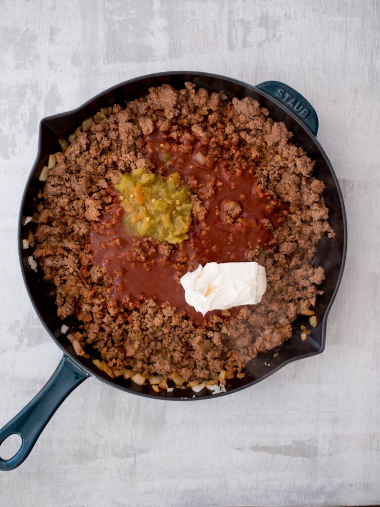 Ground beef in a cast iron pan and seasonings added to the meat to combine.