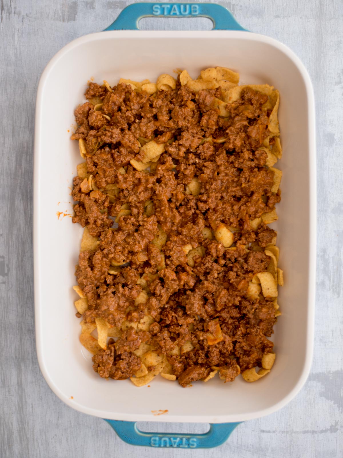 Baking dish with fritos and seasoned meat topping it.