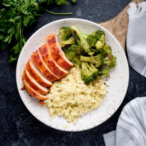 Sliced smoked chicken breasts plated with broccoli and rice.