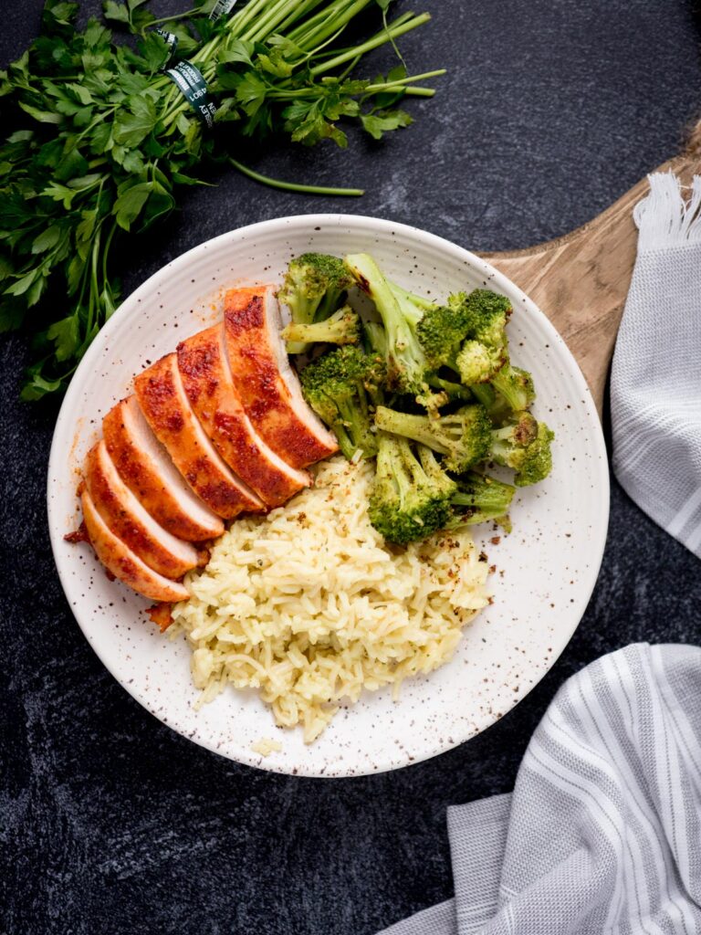 Smoked chicken sliced and plated served with broccoli and rice.
