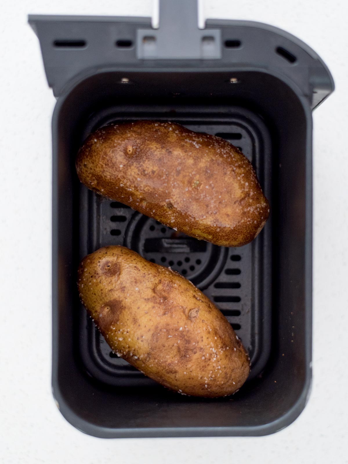 Two whole potatoes inside an air fryer.