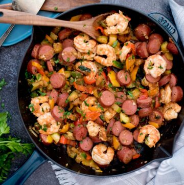 Scoop of cajun shrimp, sausage and vegetables on a wooden spoon in a cast iron pan.