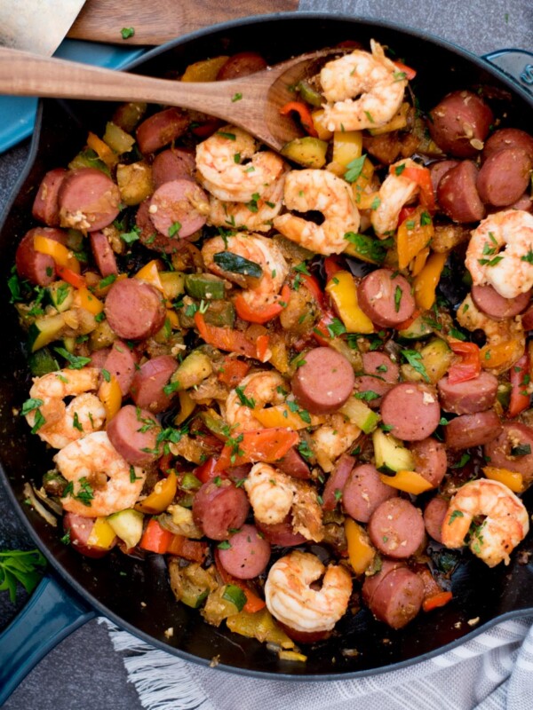 Scoop of cajun shrimp, sausage and vegetables on a wooden spoon in a cast iron pan.
