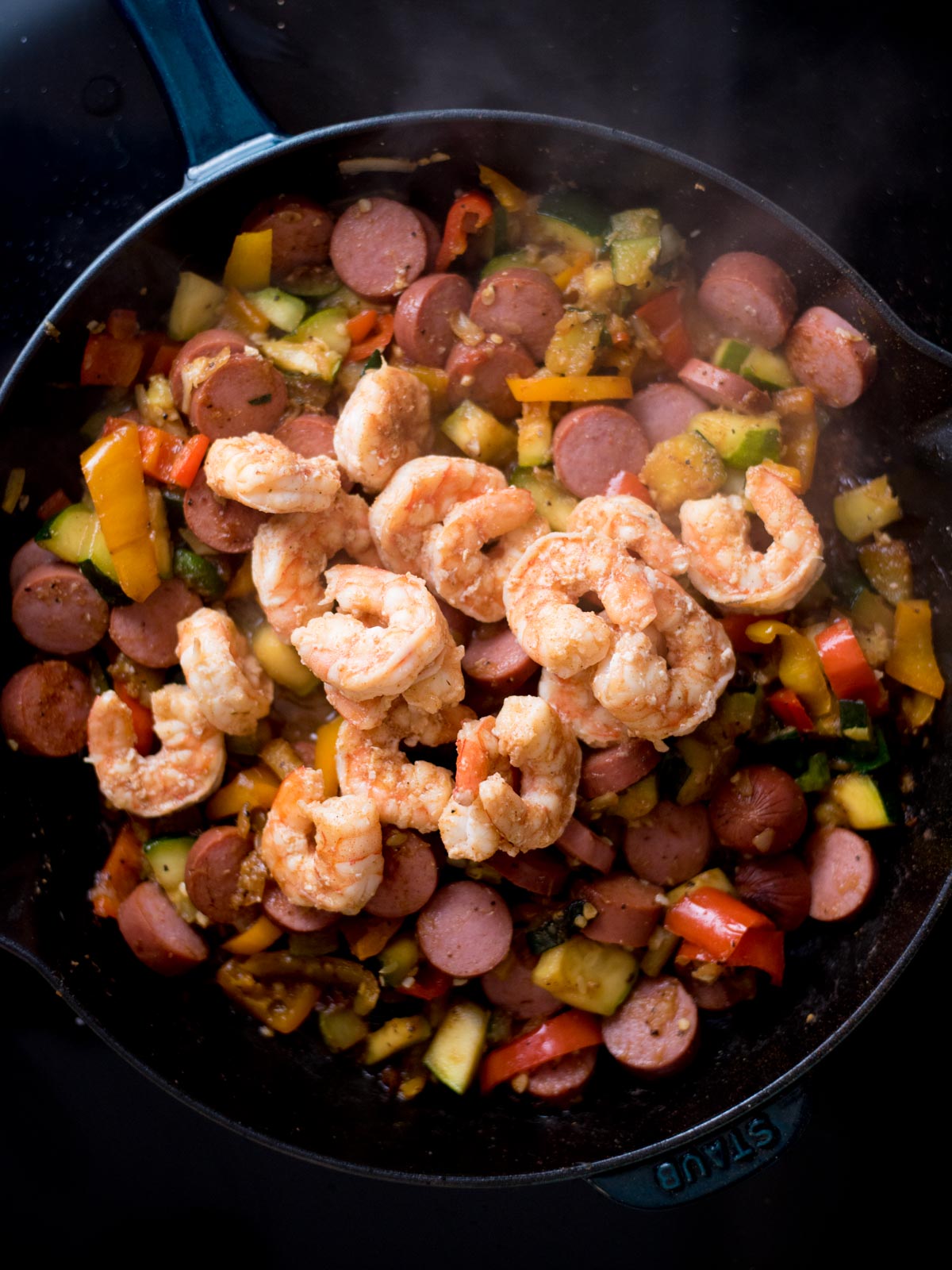 Shrimp added to cooked sausage and veggies in a cast iron skillet.