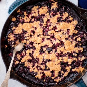 cherry crisp in a cast iron skillet with a spoon scooping it out