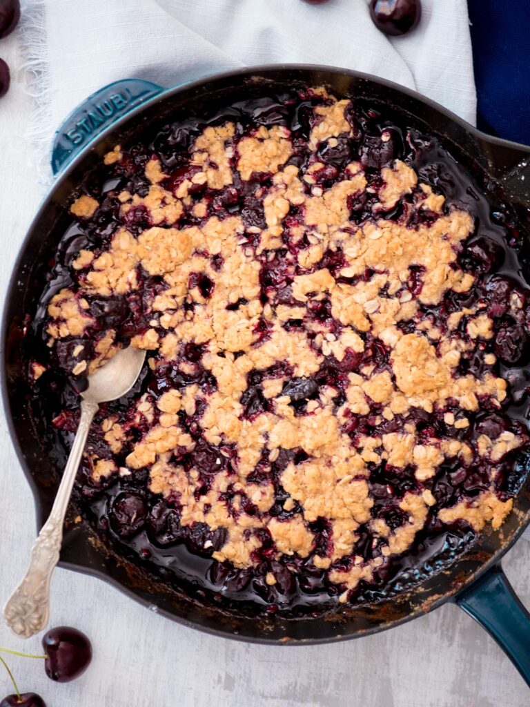 cherry crisp in a cast iron skillet with a spoon
